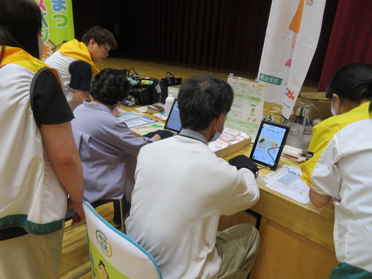 健診会場で野菜摂取量を測定する参加者と説明するスタッフの様子