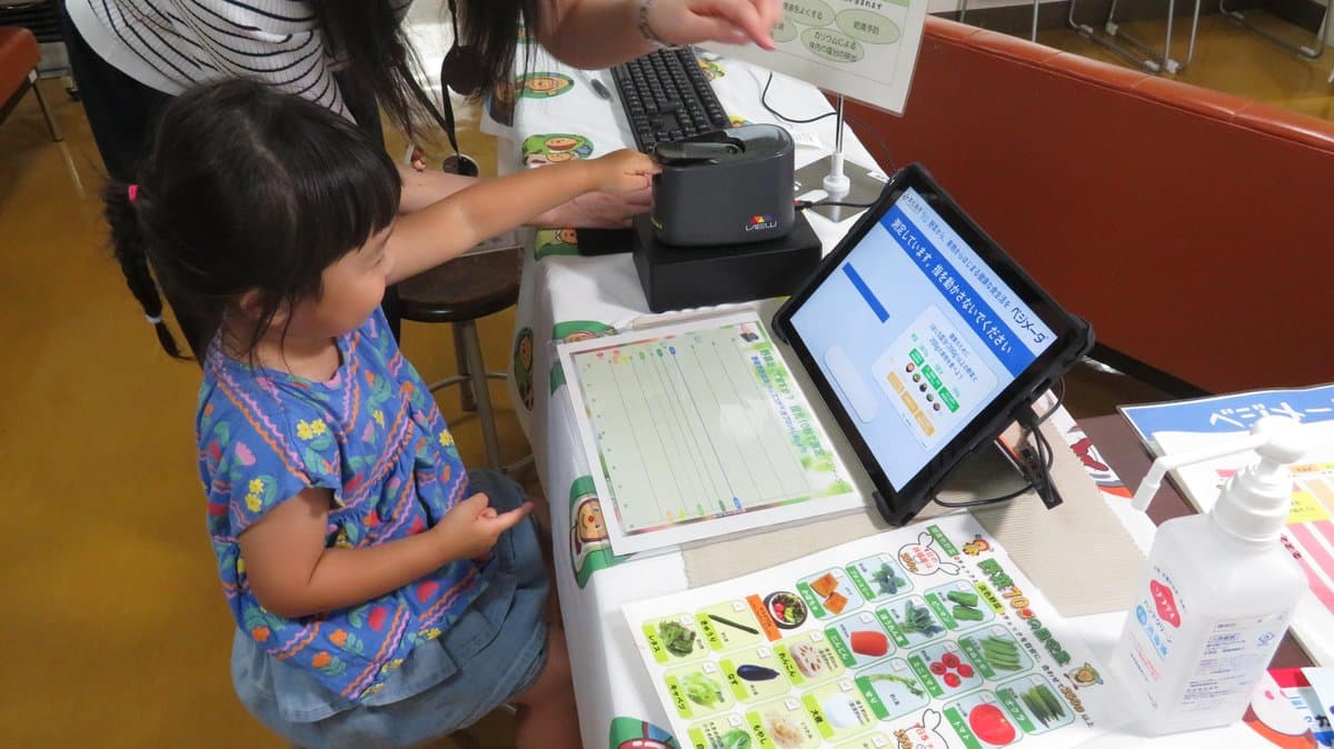 測定器に指先をのせて野菜の摂取状態を測る子ども