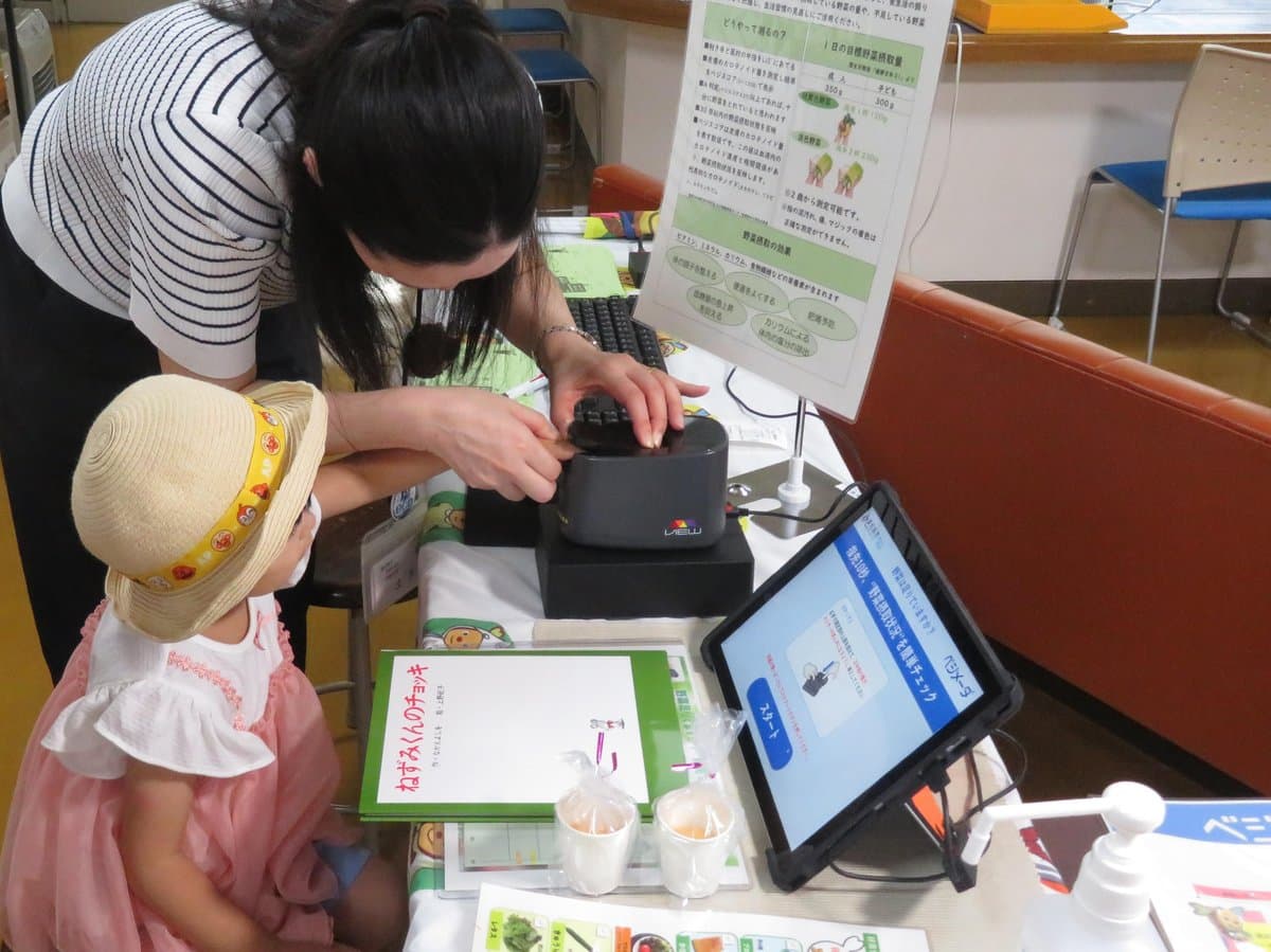 保護者に手を添えてもらいながら測定器に指をのせる子ども